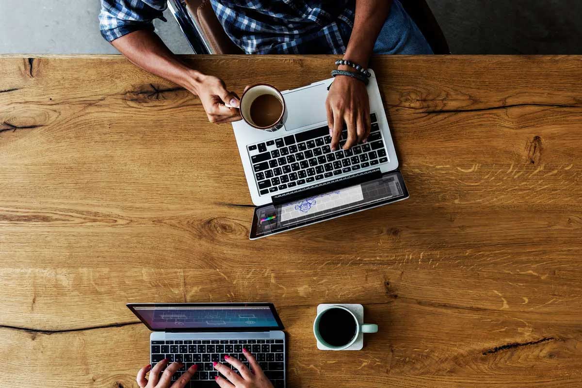 Overhead shot of laptops on wood table with people working and drinking coffee